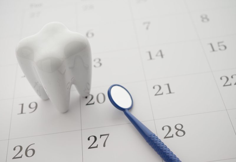 White healthy tooth model and dentist mirror on blank white calendar background with copy space. Dental appointment or schedule, dental care, healthcare, dental insurance concept.
